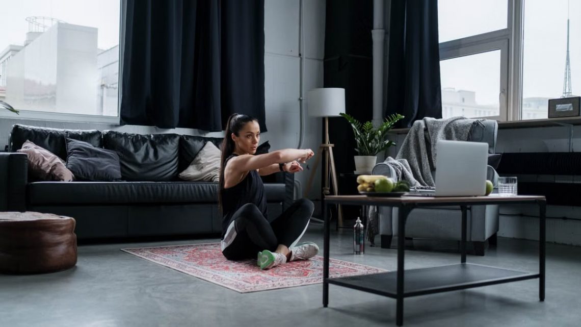 Woman doing exercise at home, sitting and stretching in a cozy living room.